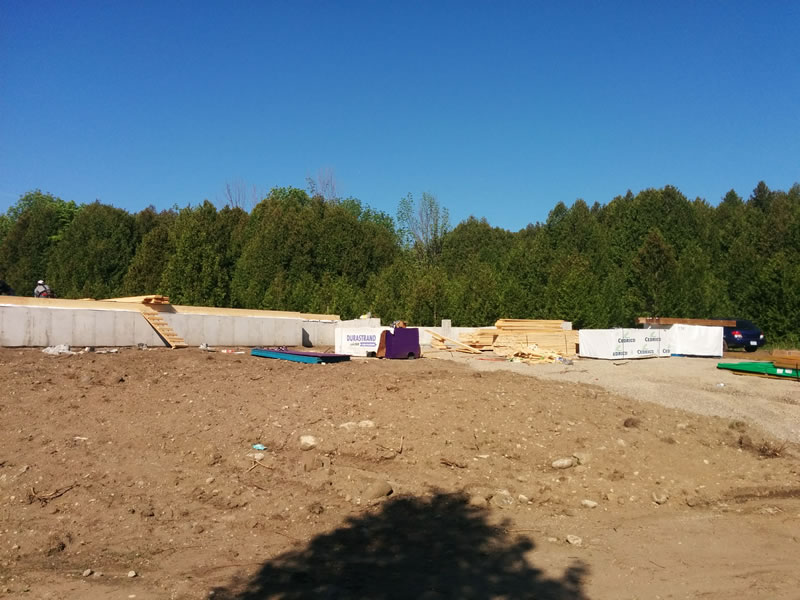 Poured foundation walls and a lumber delivery on a cleared lot at the start of an A&R build