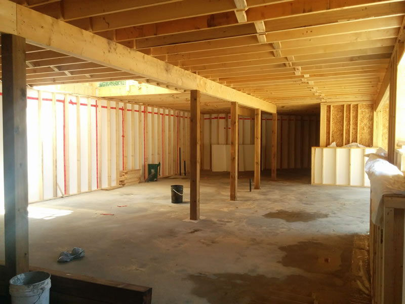 Inside a lower level under construction: a concrete floor, framed exterior walls and wood posts carrying the beam for the floor above