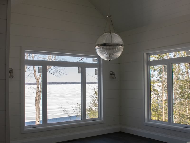 A corner room in the Crandon with two window walls looking out over a frozen Muskoka lake, white shiplap and a globe pendant under a vaulted ceiling