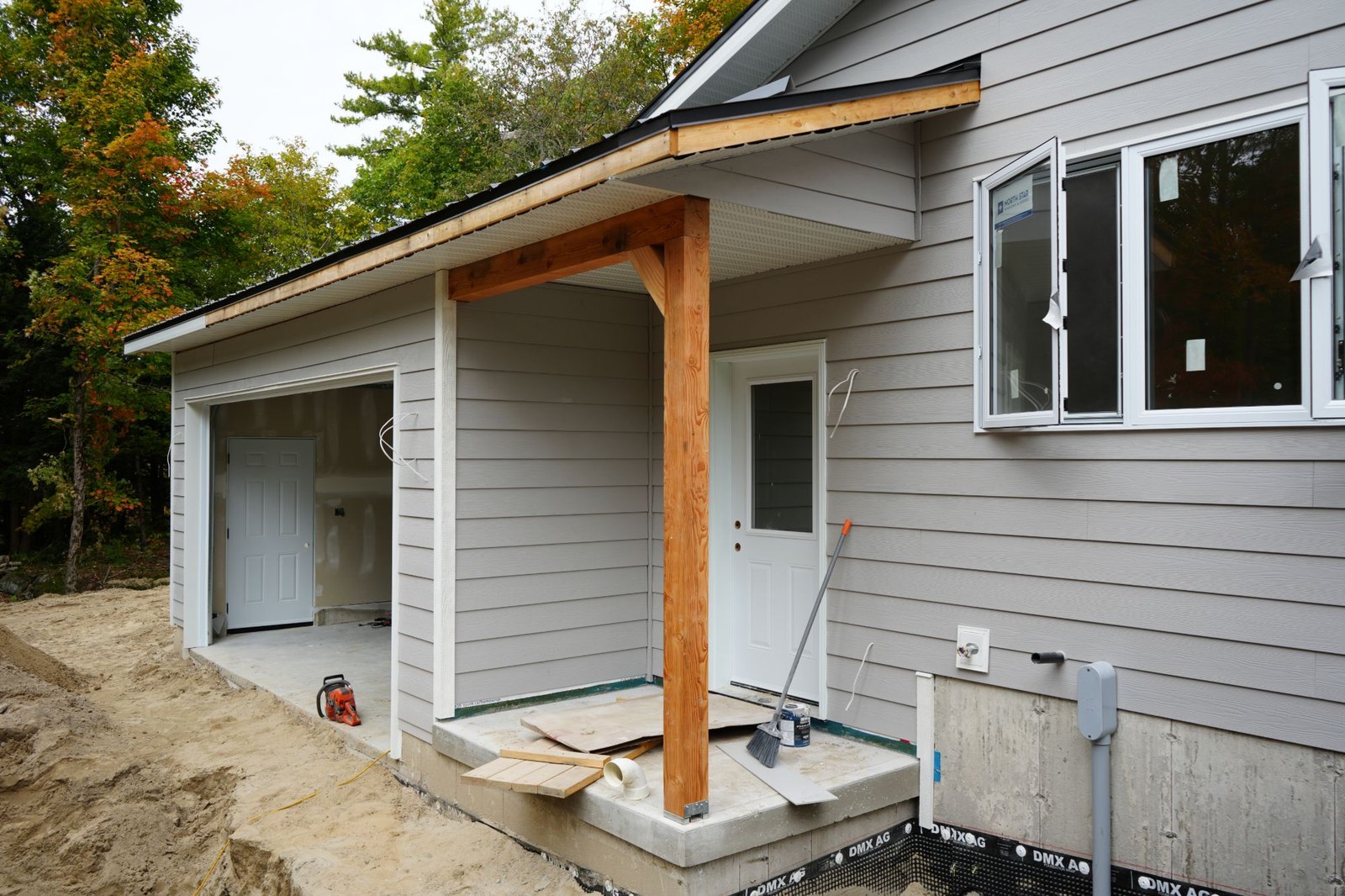 Foundation stage of a house under construction in autumn: concrete walls in dimpled membrane below the garage and covered entry, before backfill, the stage at which a frost wall is still in view