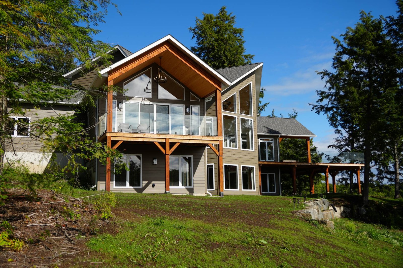 Rear of a lakeside home on falling ground, a cedar gable porch above and the lower level walking out to the lawn, where the foundation has to follow the slope down