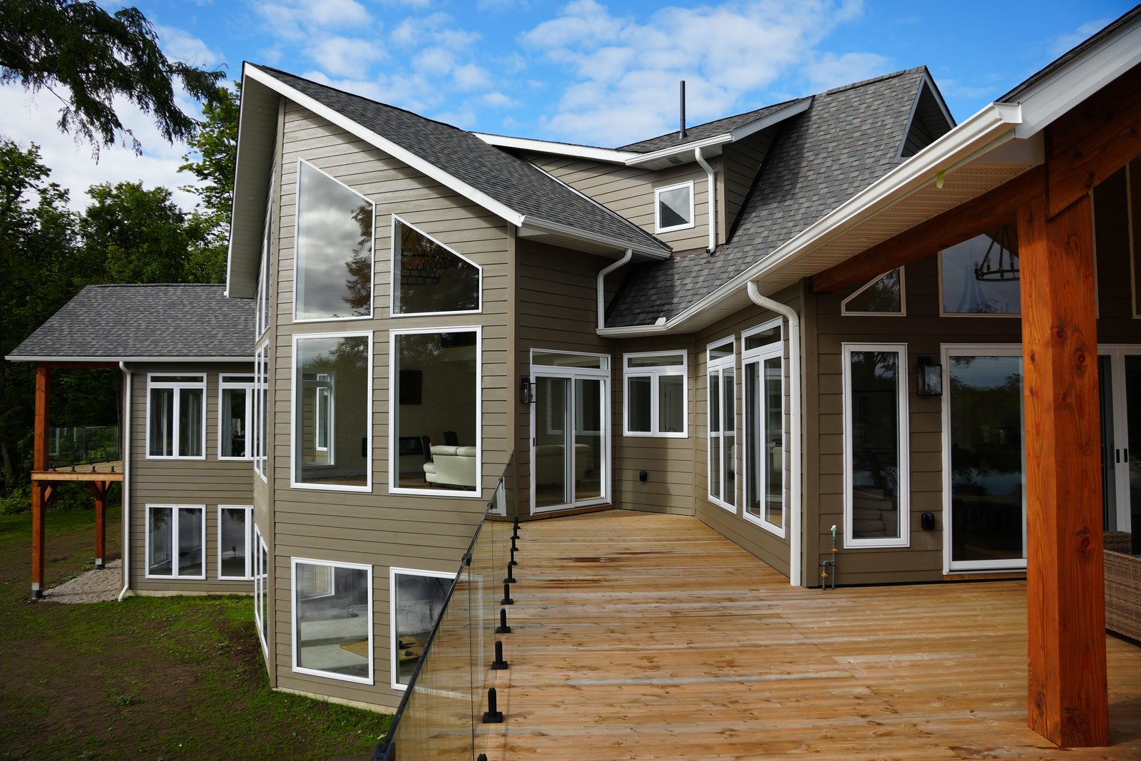 A steep gable wall on a finished lakeside home, mostly glass from the deck up to near the peak, with a glass-railed deck in front