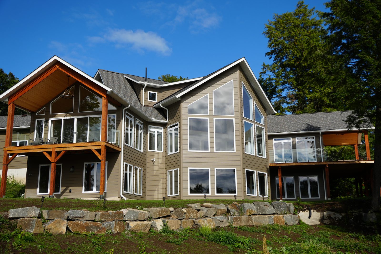 A finished A&R lakeside home with a steep timber-framed gable over a two-level deck, heavy wood posts and braces carrying it, and a tall glass-filled gable wall beside it