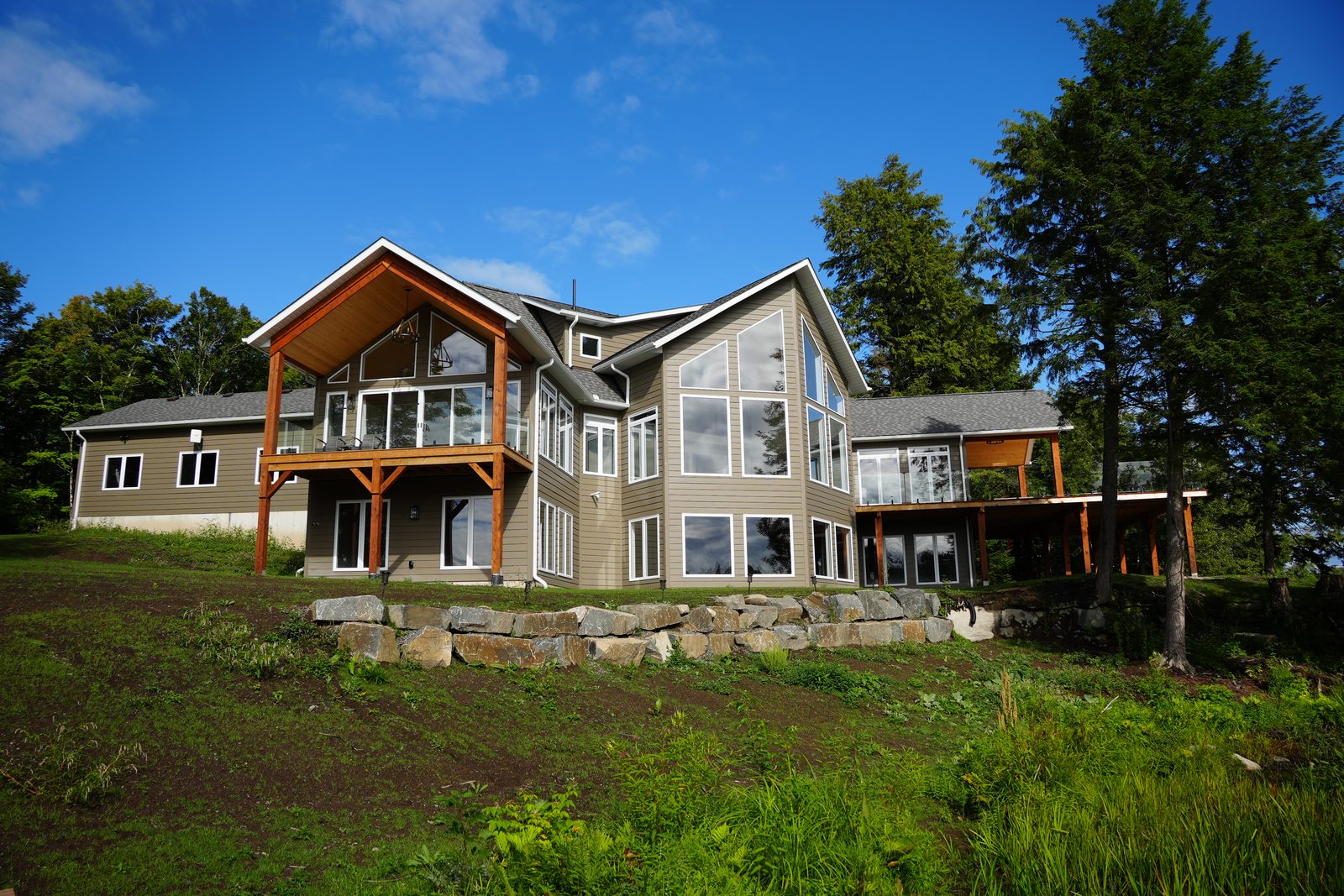 A finished A&R waterfront home on falling ground: bare concrete foundation wall showing on the high side, and the lower level opening out at grade beneath the decks on the low side