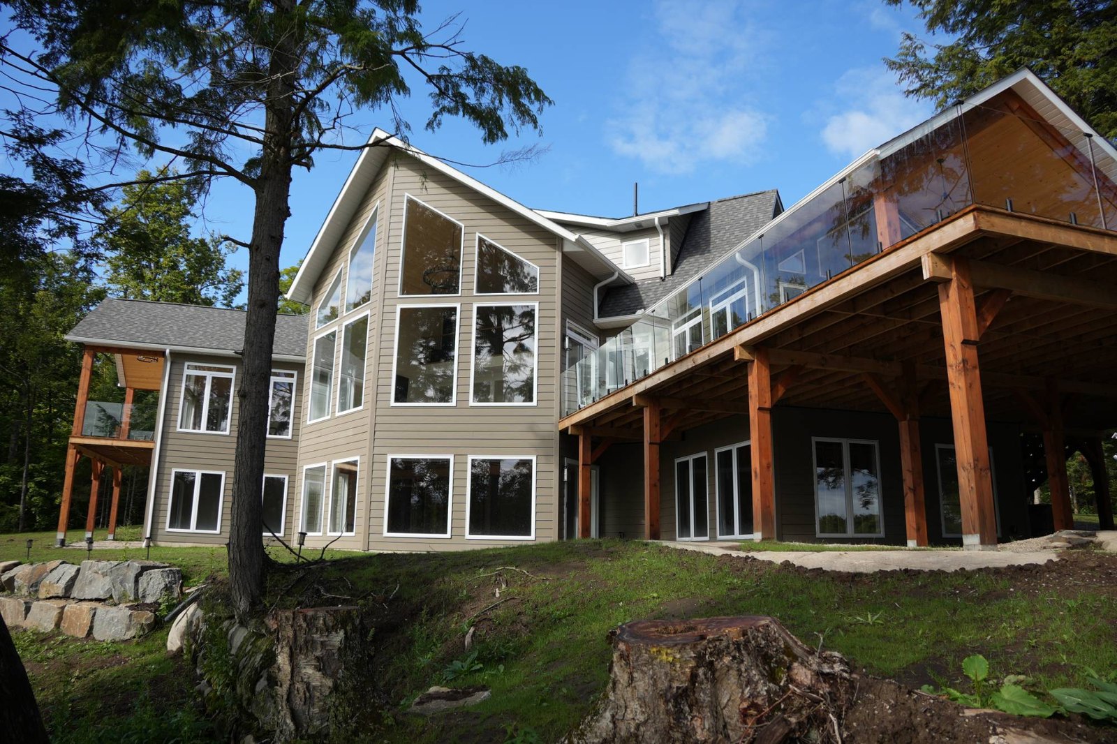 The rear of a lake house with a tall gable wall of windows above a covered deck carried on timber posts