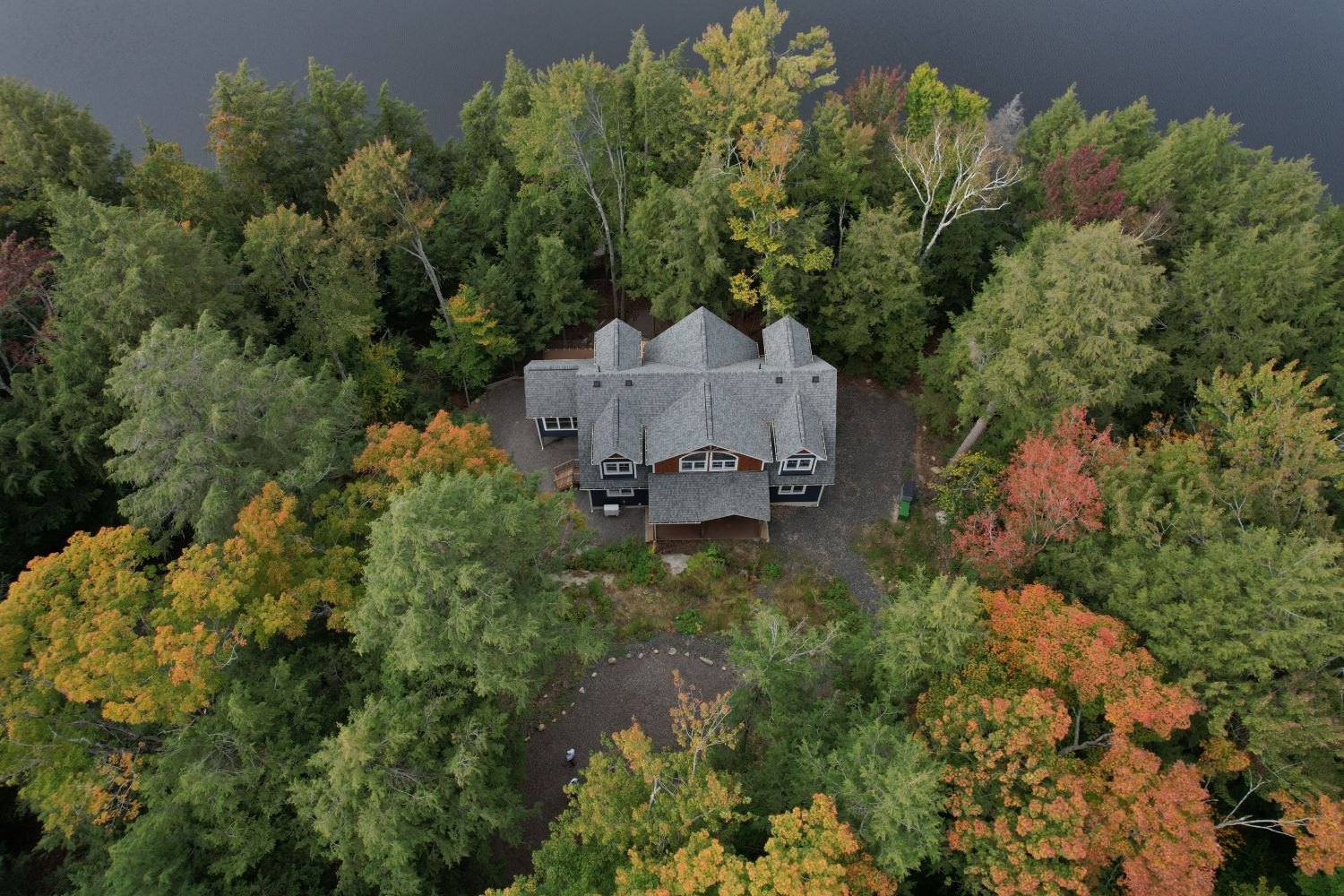 An aerial view of a house and its grey roof surrounded by tall mixed forest in autumn colour