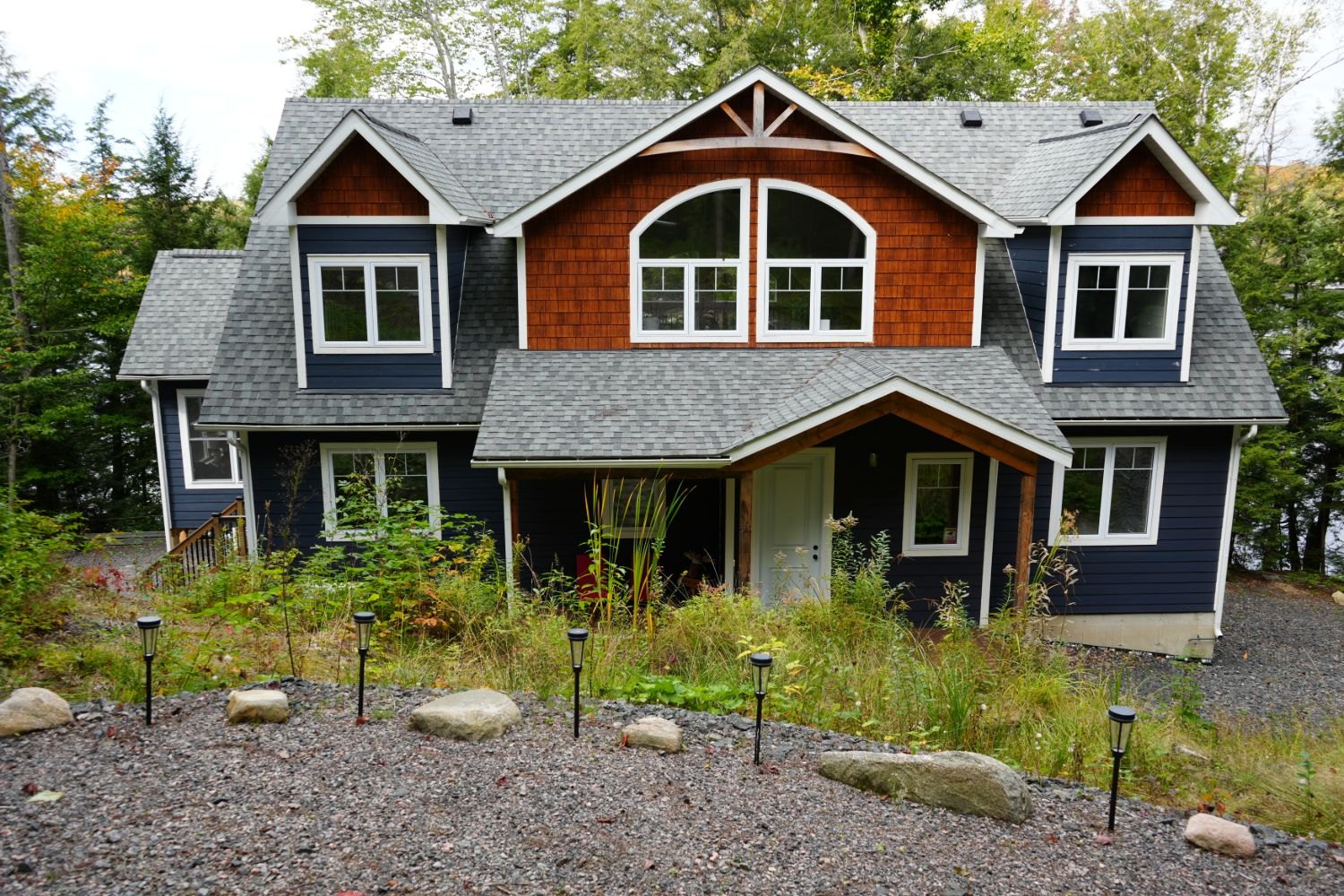 A two-storey house with cedar-shake gables and a grey shingled roof seen whole from the front, the shell of walls, roof and windows that net zero homes are judged on