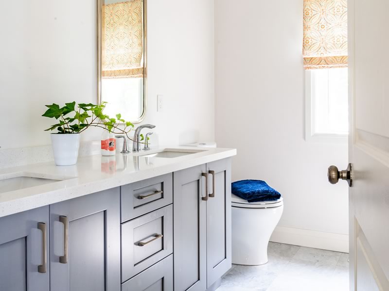 A bathroom vanity in the same home: grey shaker cabinetry with brushed nickel bar pulls, a white quartz top with an undermount sink, and a roller blind at the window