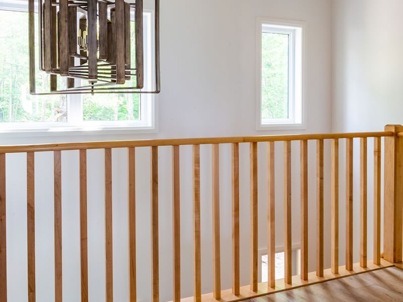 An upper-floor guard of evenly spaced vertical wood balusters along an open stairwell, with a tall window and a wood-framed pendant light behind it